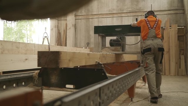 worker gives the desired shape to a wooden beam on planer machine, the construction of wooden houses, Russia june 2018