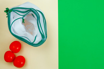 The reusable organza net bags for shopping with tomatoes are on green yellow background. Concept of no plastic, zero waste, reusable life. Flat lay. Copy space.