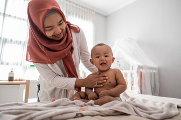 muslim mother giving a baby boy massage during diaper change