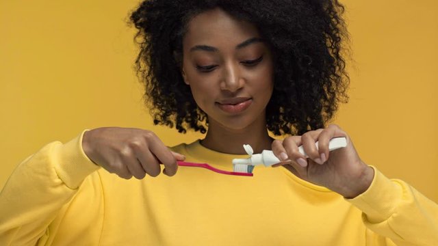 smiling african american woman squeezing toothpaste isolated on yellow