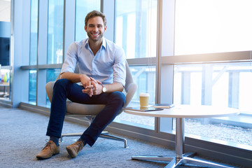 Friendly young businessman sitting casually in modern corporate space