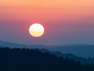 Fototapeta premium Sunset in the mountains with full disk of sunset under the horizon. Magical sunset in the Carpathians, orange sky, full disk of sunset. 