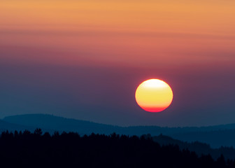 Sunset in the mountains with full disk of sunset under the horizon. Magical sunset in the Carpathians, orange sky, full disk of sunset. 