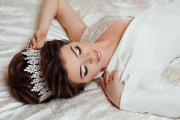 Obraz na płótnie Canvas Beautiful sexy and fashionable brunette bride in white lying on the bed in the bedroom - wedding preparation of the young stylish bride. Morning of the bride.