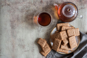 Chocolate crackers on a white plate, a Cup of tea, a glass teapot with hot tea on a gray background
