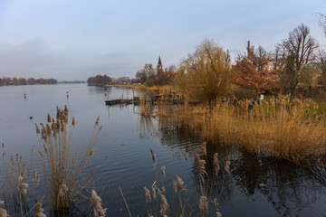 The charming and romantic small town of Werder with a church lies on the Havel River in Germany. It is a beautiful winter afternoon. In the foreground are beautiful trees and a jetty.