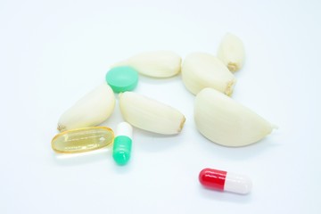 Garlic cloves and tablets located on a white background