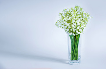 Bouquet of lilies of the valley in a glass vase on a blue background, copy space