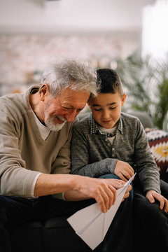Grandfather teaching his grandson how to make paper airplane. Grandpa and grandchild playing together. 