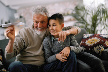 Grandfather teaching his grandson how to make paper airplane. Grandpa and grandchild playing together. 