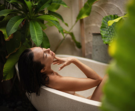 Woman relaxing in outdoor bath with tropical leaves at Bali