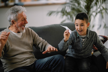 Grandfather teaching his grandson how to make paper airplane. Grandpa and grandchild playing together. 