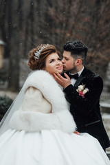 Sensual and tender bride and groom outdoors on wedding day. Bride wearing gorgeous wedding dress with lace and long veil. Wedding couple in winter. Groom and bride together. Winter wedding