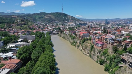 Fototapeta na wymiar Aerial view of Kura river in Old Town of Tbilisi, Georgia. Church, Houses, trees, mountain ad blue sky. Summer. Travel destinations.