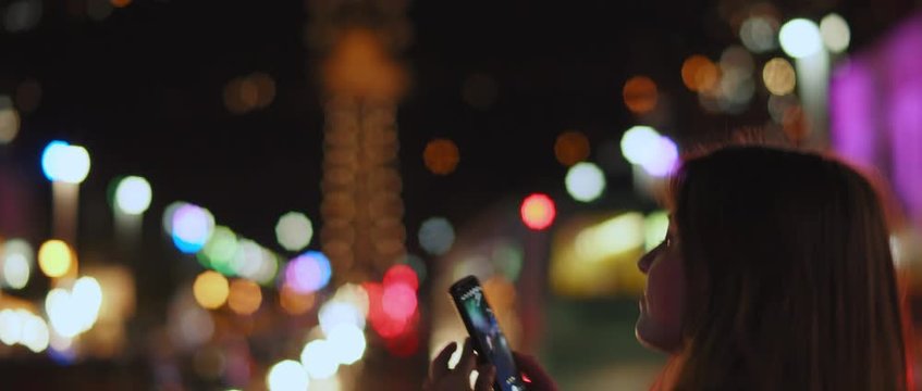 A young woman taking picture of a night city in the middle of a street, bokeh lights on the background. Shallow dof, realtime, BMPCC 4K