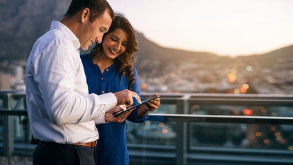 Diverse colleagues standing on an office balcony using a tablet