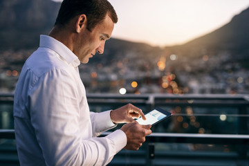 Focused businessman standing on an office balcony using a tablet