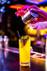 Bartender finishes preparation of cocktail in crystal glass by adding a bitter of cinamon powdered. Close-up of expert bartender making cocktail in bar.