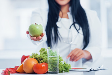 Female nutritionist in white coat holding apple in hand