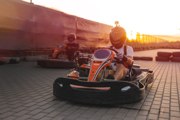 Two racers on karts are approaching the finish line in an active battle for first place in the championship, sreet, rent. extreme sport. fun entertainment for drivers, sunset soft light - obrazy, fototapety, plakaty