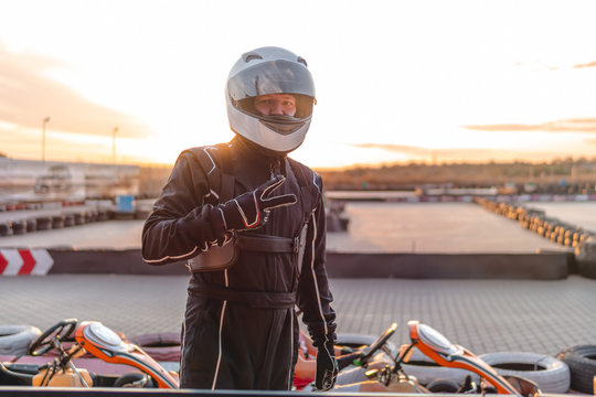 The driver of a racing car stands in the center of the photo. Equipped in racing overalls, helmet and gloves. posing. at sunset. Go karts racing,, rent. extreme sport. fun entertainment for drivers