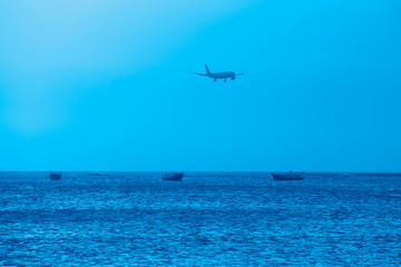 Fototapeta na wymiar Beautiful seascape with an airplane in the sky in the trendy classic blue color of the year.