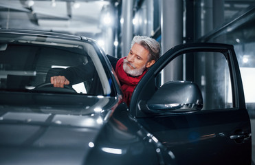 Stylish senior man with grey hair and mustache sitting into brand new modern car