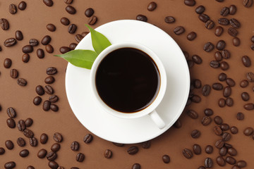 Coffee beans and a cup of coffee on a brown color background. Top view. Place for text.