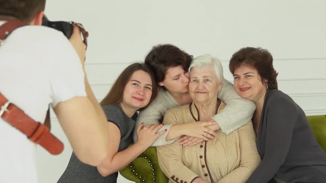Photographer is taking pictures of an elderly white-haired woman with her granddaughters. The beautiful multi-generations family enjoys togetherness 