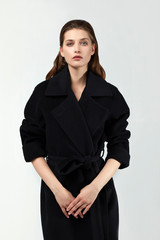 blue eyed brown haired pretty young model standing and posing in her black luxurious coat. white background. standing.