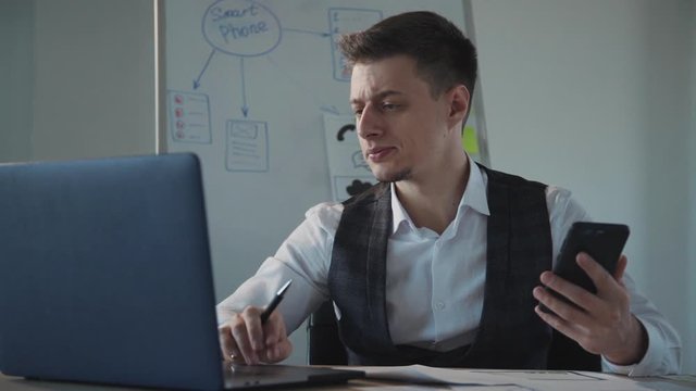creating interface design. concept of ux design. white boad with smartphone inscription on background. business man working on laptop, checking his phone and drawing on a paper with pen