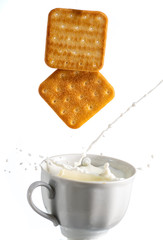 two cookies fall in a mug with milk and a splash on a white background