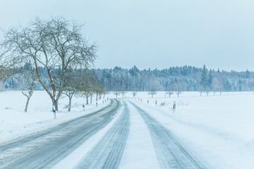 Obraz premium Lonely slippery icy winter road traffic with white snowy track. The street track is slick frozen. High dangerous risk of accident through blizzard snowstorm and severe christmas time season weather