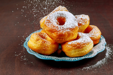 Sprinkle homemade donuts with sugar powder on blue dish.