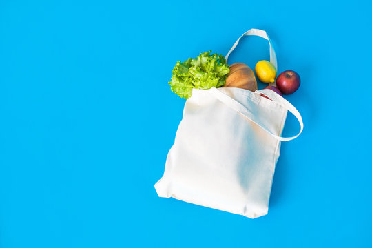 Cotton eco-bag with green fresh kale and fruits on the blue background.