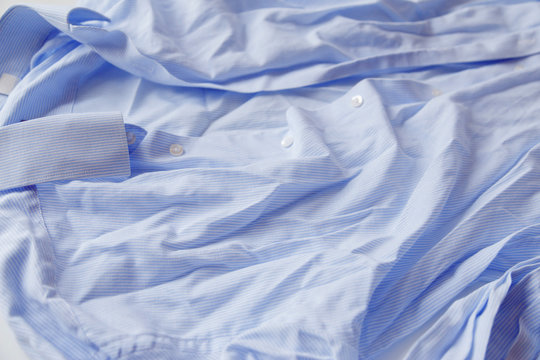 Blue cotton wrinkled and rumpled shirt on white. Washed shirt after tumble dryer