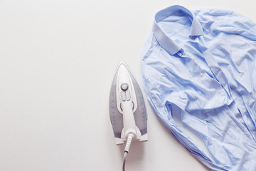 Blue cotton wrinkled and rumpled shirt ironing with iron. Tumble dryer after washing machine.