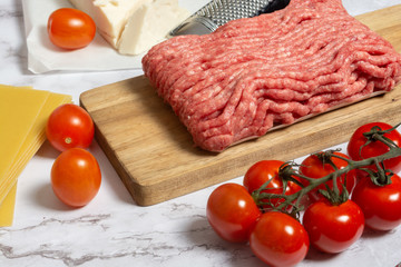 Close up view of minced meat with lasagna sheets, parmesan cheese, bottle of olive oil and vegetables for preparing Italian pasta 