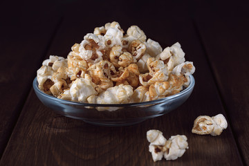 Popcorn in a transparent glass plate on a wooden background