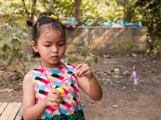 Asian child girl playing, blowing bubbles outdoor with happy relaxing face  with natural rural green background and bubbles in the air. Young kid have fun in holiday.