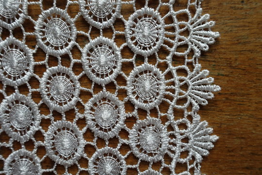 Close view of edge of ivory white crochet lace on wooden table
