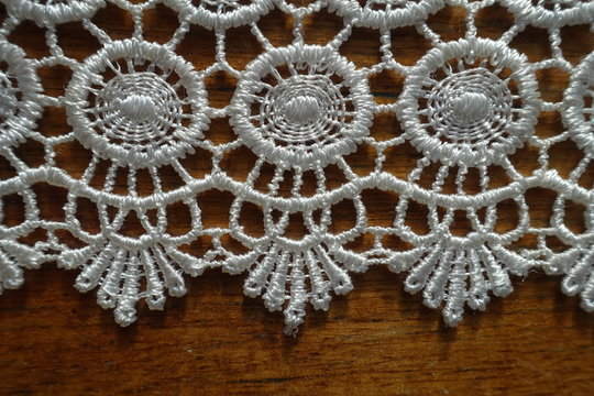 Closeup of edge of ivory white crochet lace on wooden table