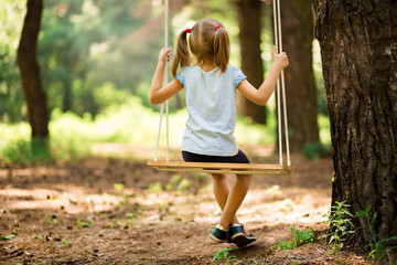 Happy Little girl on a swing in the summer park