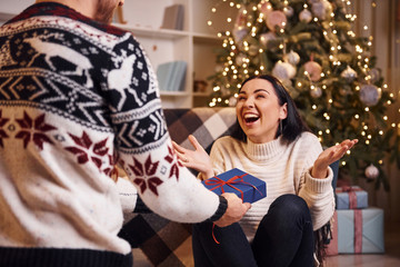 Man covers eyes of hir girlfriend and giving new year surprise in christmas decorated room