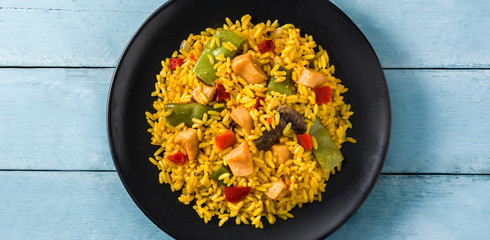 Fried rice with chicken and vegetables in black plate on blue wooden table. Top view. Panorama view