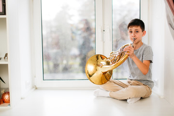 Caucasian boy learns to play horns, light window