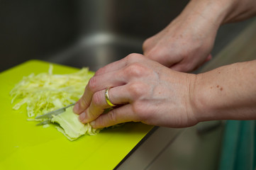 Married woman wearing wedding ring slicing cabbage on top of a green cutting board. Horizontal shot.