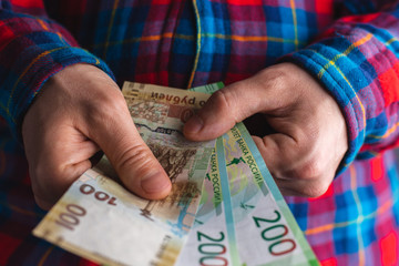 man in a red and blue plaid shirt counts money in hands. Man hands holding pile of money. counts money in hands. Russian 200 Ruble currency