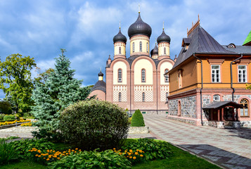 Fototapeta na wymiar Kuremäe, Estonia - Pyuhtitsky monastery of the Russian Orthodox Church, a red and yellow brick church with black domes, a garden with orange flowers, a blue sky with clouds.