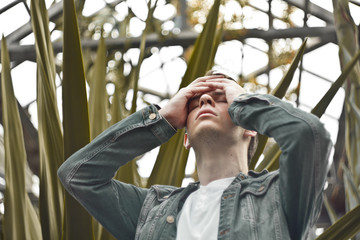 Handsome man in depression. Not shaved hipster in a botanical garden, holding on to his head. Concept: headache and grief.